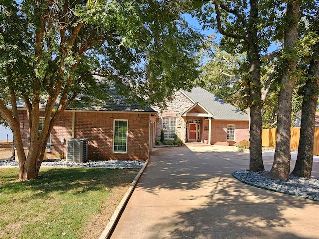 view of front of house with brick siding, central AC unit, fence, driveway, and a front lawn