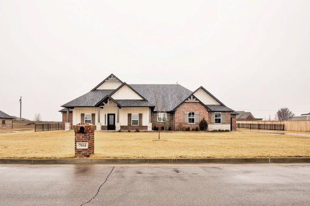 view of front facade featuring a shingled roof, a front yard, brick siding, and fence