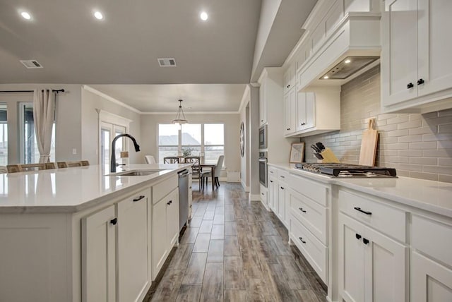 kitchen with a center island with sink, decorative backsplash, custom exhaust hood, stainless steel appliances, and a sink