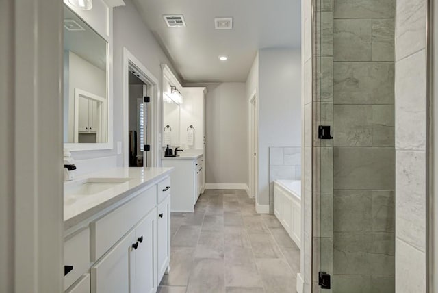 bathroom with a garden tub, two vanities, a sink, visible vents, and baseboards