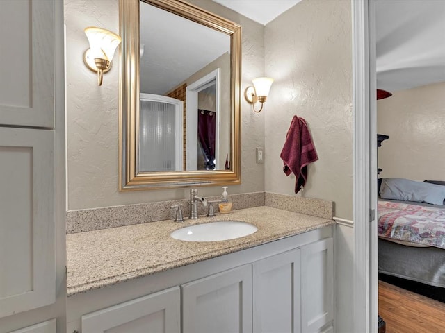 bathroom featuring a textured wall, ensuite bath, wood finished floors, and vanity