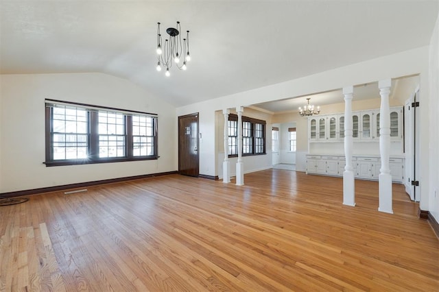 unfurnished living room featuring lofted ceiling, a notable chandelier, light wood finished floors, and ornate columns