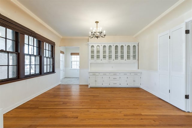 unfurnished dining area featuring crown molding, baseboards, a notable chandelier, and light wood finished floors