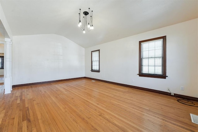 empty room featuring light wood-style flooring, visible vents, baseboards, vaulted ceiling, and decorative columns