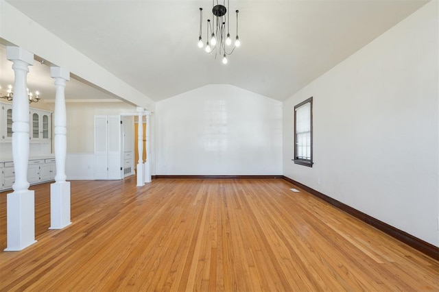 empty room featuring light wood finished floors, baseboards, an inviting chandelier, vaulted ceiling, and ornate columns