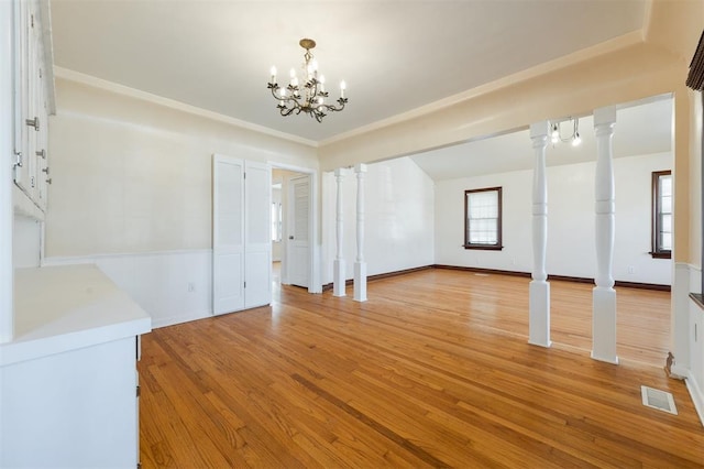 unfurnished dining area featuring an inviting chandelier, decorative columns, visible vents, and light wood-style flooring