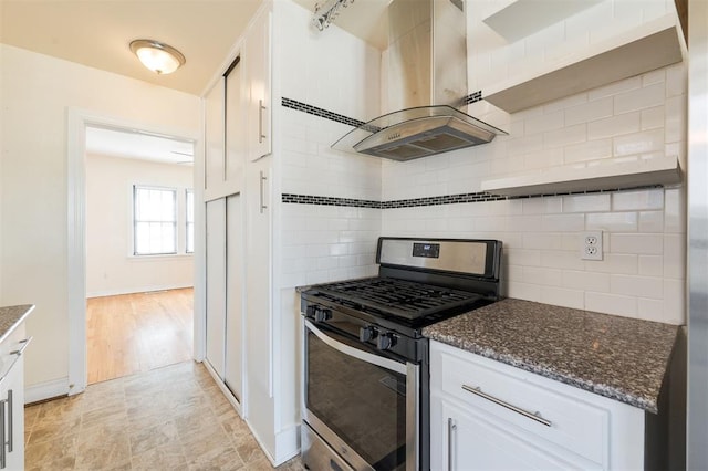 kitchen featuring stainless steel gas range oven, white cabinetry, decorative backsplash, dark stone countertops, and island exhaust hood