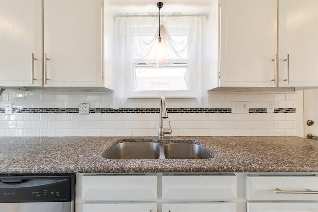 kitchen with decorative backsplash, dark stone counters, a sink, white cabinetry, and stainless steel dishwasher