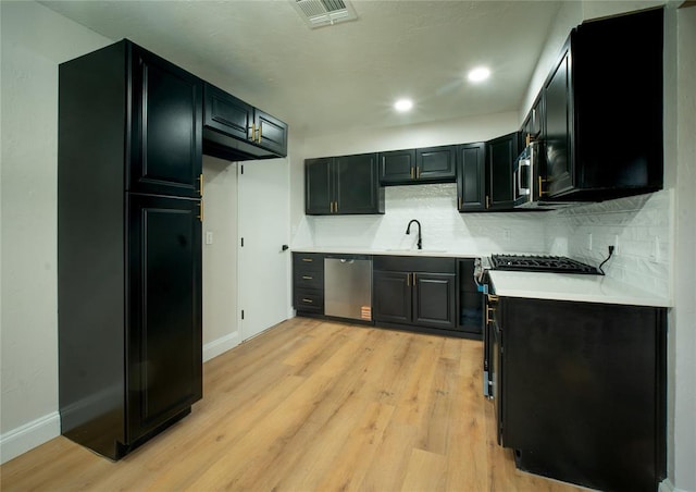 kitchen with light wood finished floors, stainless steel appliances, visible vents, backsplash, and a sink