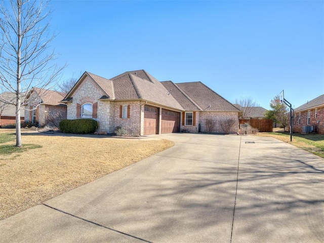 french country inspired facade with roof with shingles, brick siding, an attached garage, stone siding, and driveway