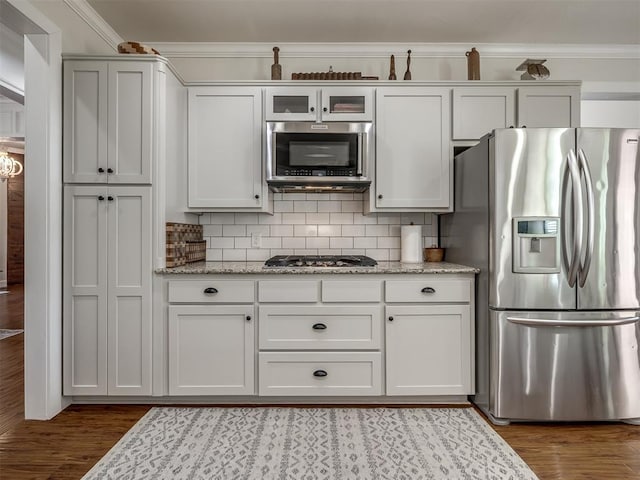 kitchen with stainless steel appliances, wood finished floors, backsplash, light stone countertops, and crown molding