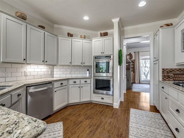 kitchen featuring ornamental molding, appliances with stainless steel finishes, decorative backsplash, light stone countertops, and dark wood finished floors