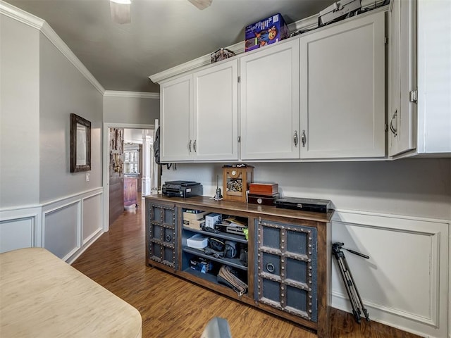 interior space with a decorative wall, wood finished floors, a ceiling fan, wainscoting, and crown molding