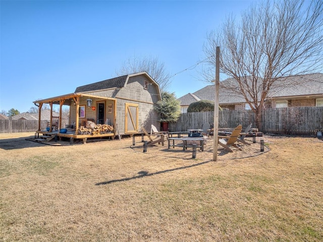 exterior space with a fire pit, a gambrel roof, an outbuilding, fence, and a yard