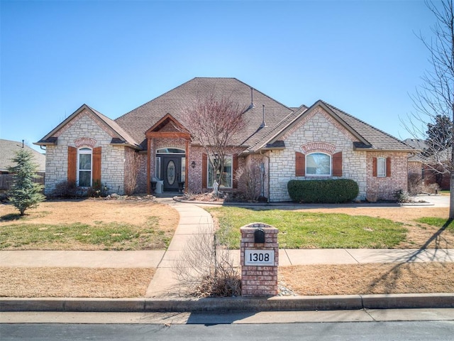 french country home featuring a front lawn and roof with shingles