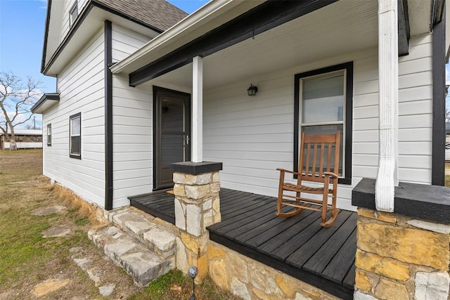 view of exterior entry featuring covered porch and roof with shingles