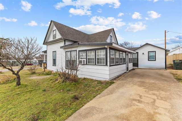 view of side of home featuring a shingled roof, a sunroom, a yard, and concrete driveway