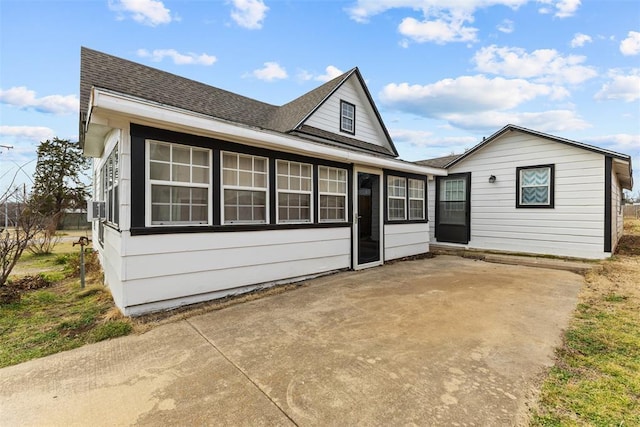 view of front of property featuring a shingled roof, a sunroom, and a patio