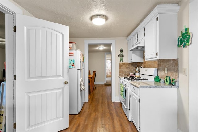 kitchen featuring white appliances, wood finished floors, white cabinets, light countertops, and decorative backsplash