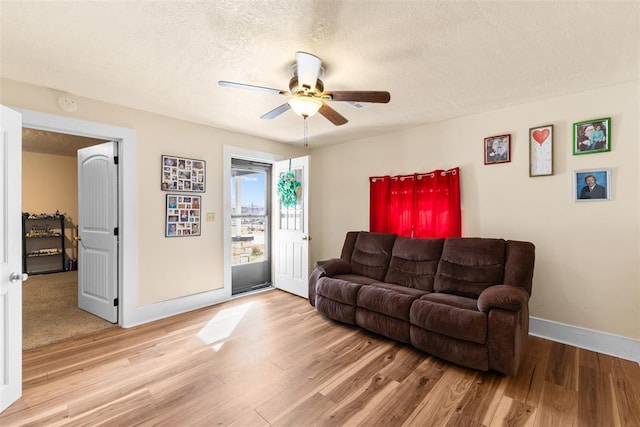 living room featuring light wood-style floors, ceiling fan, baseboards, and a textured ceiling