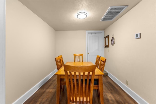 dining space featuring dark wood-style flooring, visible vents, a textured ceiling, and baseboards