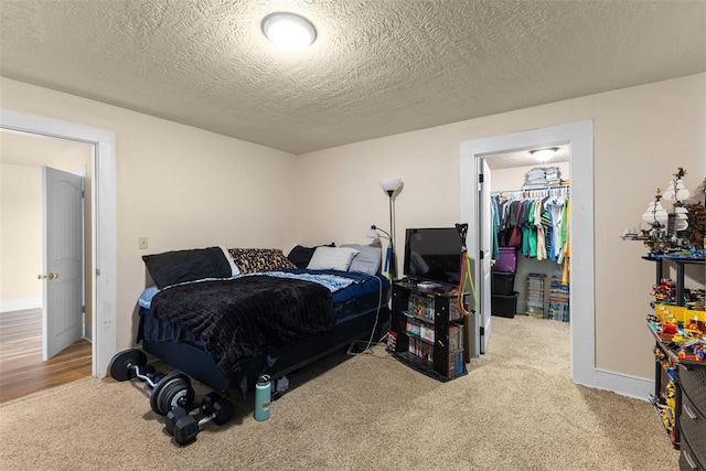 carpeted bedroom with a textured ceiling, a spacious closet, baseboards, and a closet