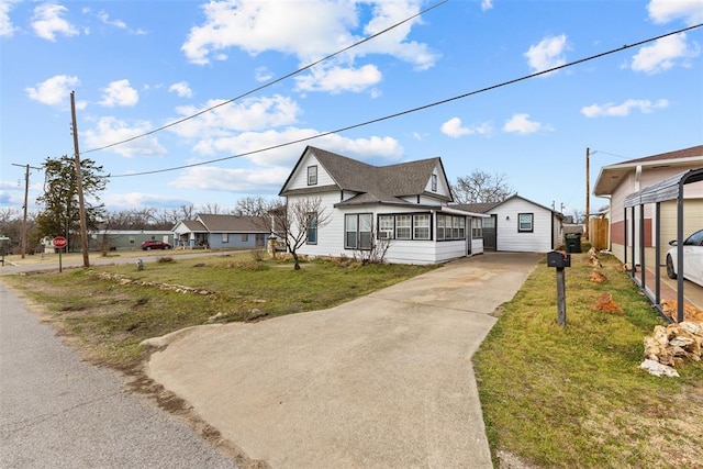 view of front of home featuring a shingled roof, a sunroom, driveway, and a front lawn