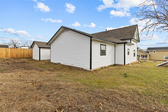 view of side of property featuring a shingled roof, fence, and a lawn