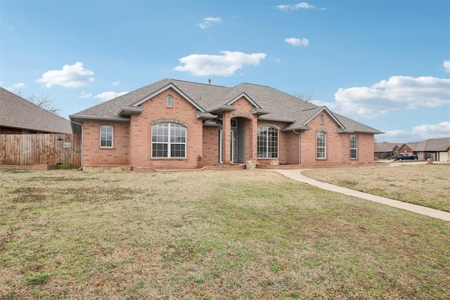 ranch-style house featuring a shingled roof, a front yard, fence, and brick siding