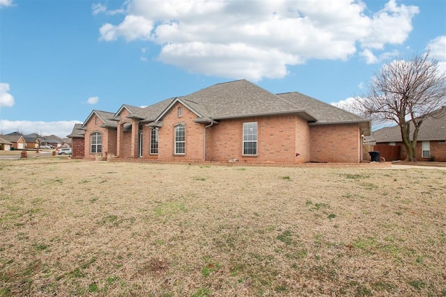 view of front facade featuring brick siding, a front yard, and a shingled roof