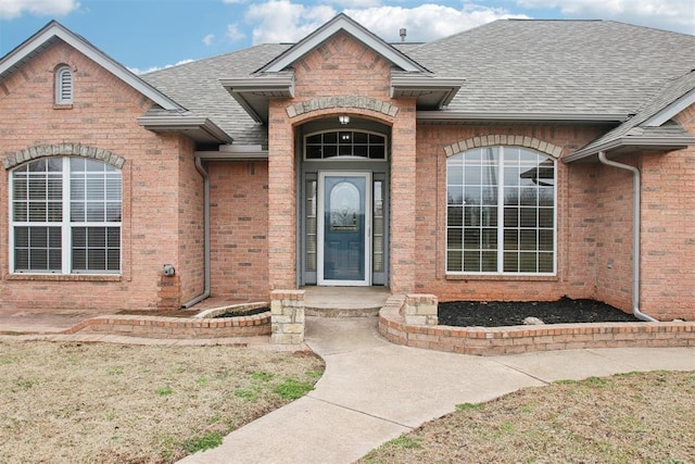 doorway to property with roof with shingles and brick siding