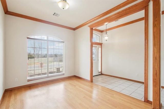 empty room with light wood-style floors, visible vents, crown molding, and baseboards