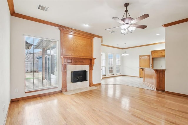 unfurnished living room with light wood finished floors, a premium fireplace, visible vents, and crown molding