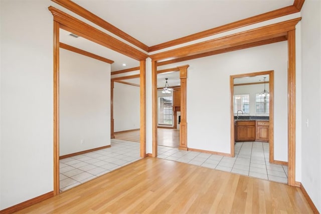 empty room featuring a sink, visible vents, a ceiling fan, ornamental molding, and light wood finished floors