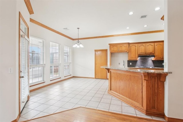 kitchen with light stone counters, under cabinet range hood, a peninsula, visible vents, and decorative backsplash