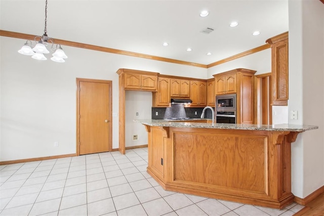 kitchen featuring light stone counters, under cabinet range hood, stainless steel appliances, a peninsula, and brown cabinetry