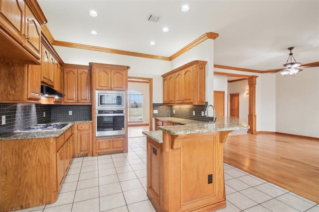 kitchen featuring light tile patterned floors, stainless steel appliances, a peninsula, under cabinet range hood, and a kitchen bar