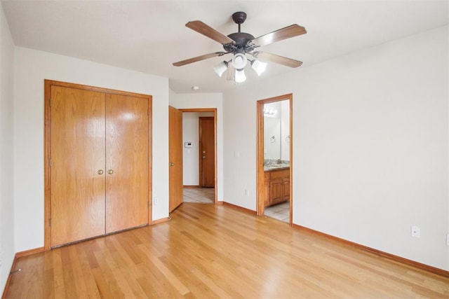 unfurnished bedroom with baseboards, a ceiling fan, ensuite bath, light wood-type flooring, and a closet