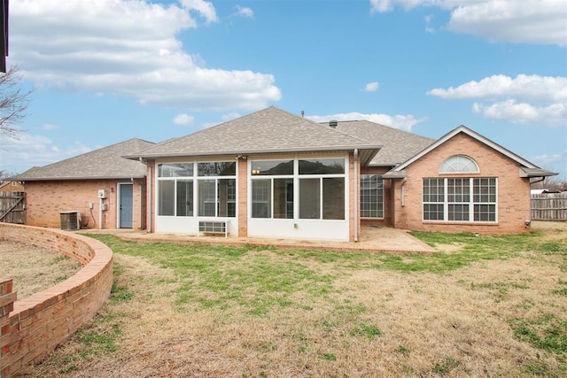 back of house with brick siding, a yard, a shingled roof, a sunroom, and fence