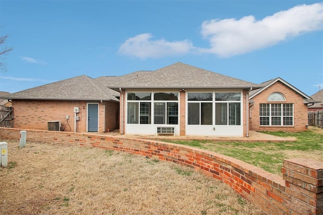 rear view of house featuring roof with shingles, a yard, brick siding, a sunroom, and fence