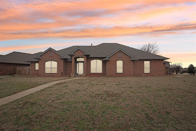 view of front of property featuring a yard, brick siding, and a shingled roof