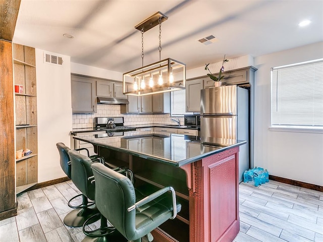 kitchen with appliances with stainless steel finishes, dark countertops, visible vents, and under cabinet range hood