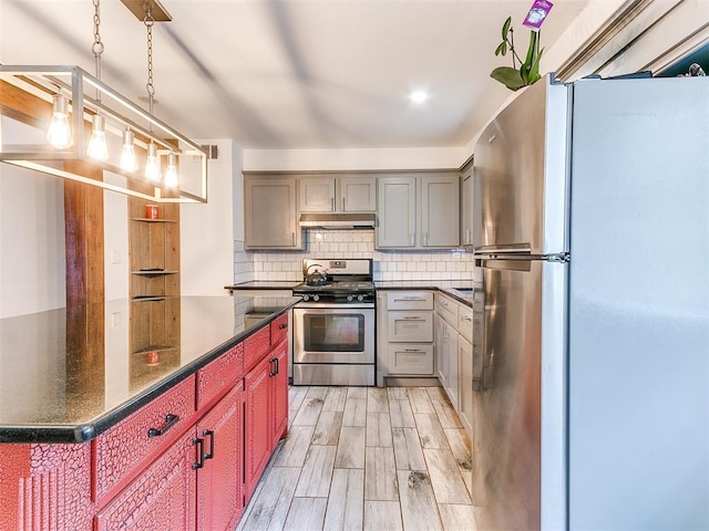 kitchen with gray cabinetry, under cabinet range hood, stainless steel appliances, wood finish floors, and backsplash