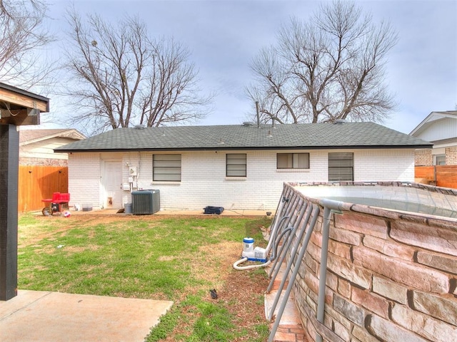 rear view of property with brick siding, a lawn, a shingled roof, and fence