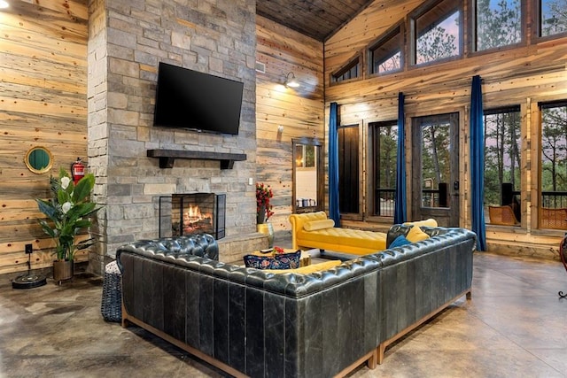 living room with wooden walls, concrete floors, high vaulted ceiling, a stone fireplace, and wooden ceiling