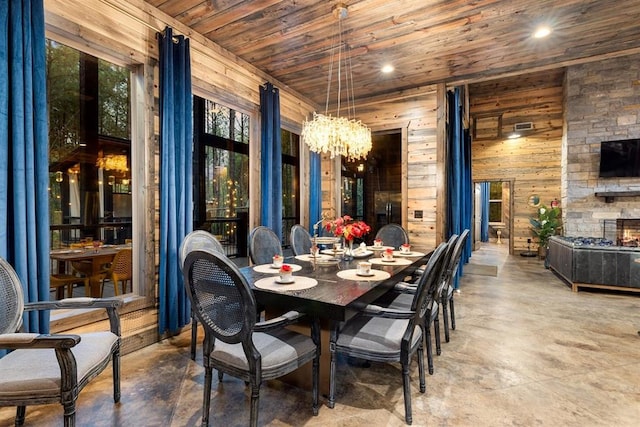 dining room featuring a fireplace, finished concrete floors, wood walls, wooden ceiling, and a chandelier