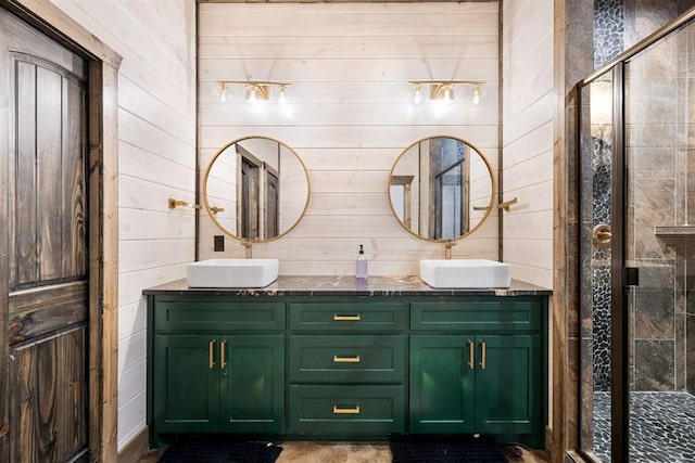 full bath featuring a shower stall, wooden walls, double vanity, and a sink