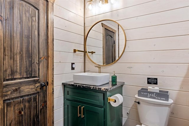 bathroom with wooden walls, vanity, and toilet