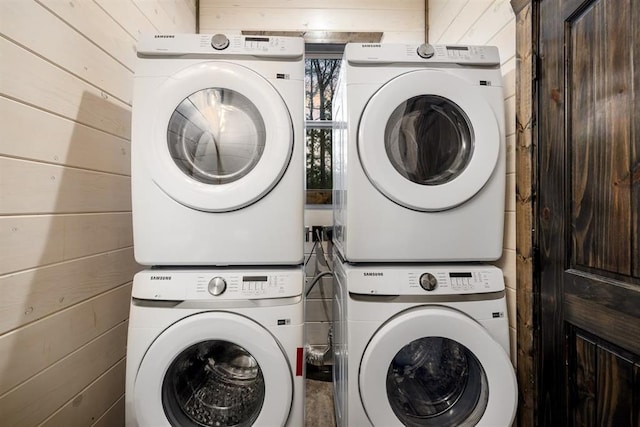 laundry room with stacked washer and dryer, wood walls, and laundry area