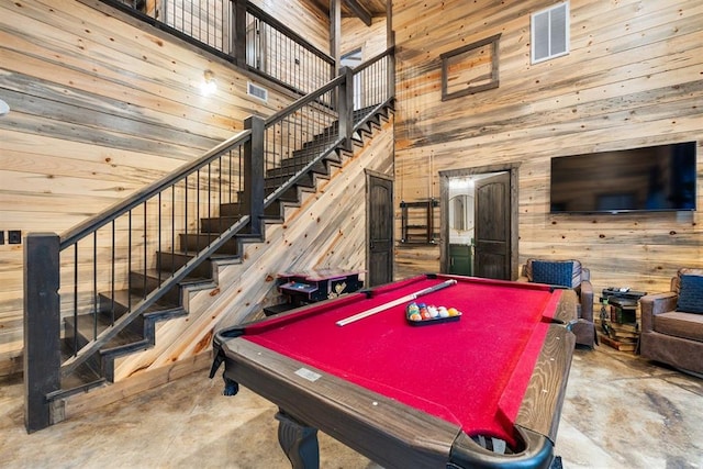 recreation room with billiards, a towering ceiling, concrete floors, and wood walls